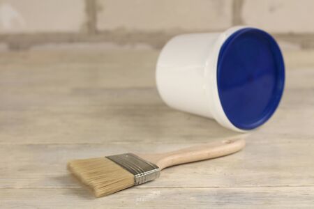 A paint brush is next to a plastic paint bucket with a blue lid on an old white vintage wooden board. Brick wall in the background. Place for text or logo.の写真素材