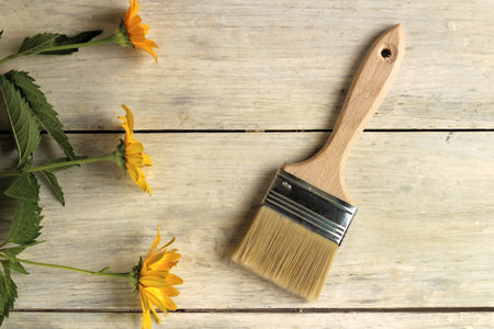 A paint brush is next to beautiful orange flowers on an old white vintage wooden plank table.