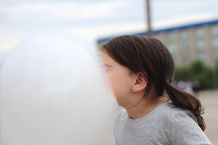 Little girl with pigtails tries to bite a big ball of cotton candy at a city celebration