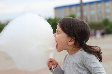 Little girl with pigtails tries to bite a big ball of cotton candy at a city celebrationの写真素材