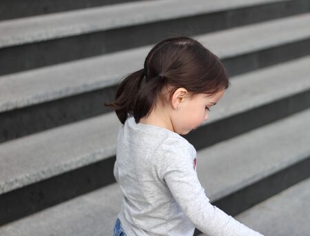 little cute white girl brunette with pigtails in jeans standing on the stairsの写真素材