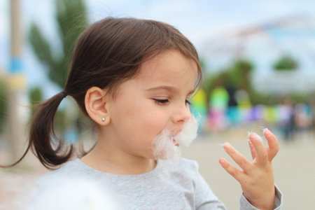 Little funny white girl with tails with narrow eyes holds cotton candy with his lips while walking...