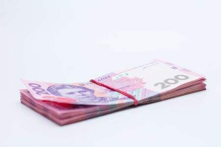 A lot of new banknotes in denominations of 200 Ukrainian hryvnias bandaged with an elastic band isolated on a white background with shadow. European money exchange. Ukraine currency. Selective focusの写真素材