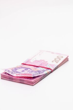 A lot of new banknotes in denominations of 200 Ukrainian hryvnias bandaged with an elastic band isolated on a white background with shadow. European money exchange. Ukraine currency. Selective focusの写真素材