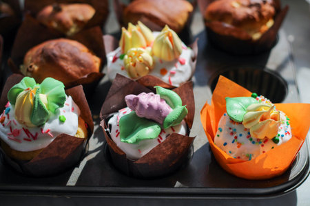 Rows of beautiful multi-colored little cupcakes in paper packaging with sprinkles and cream