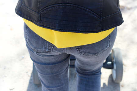 Back of a female body in tight blue jeans with pockets and a yellow sweatshirt under a leather jacketの写真素材