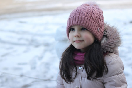 Little smiling white girl with long dark hair in a knitted hat on a background of snow