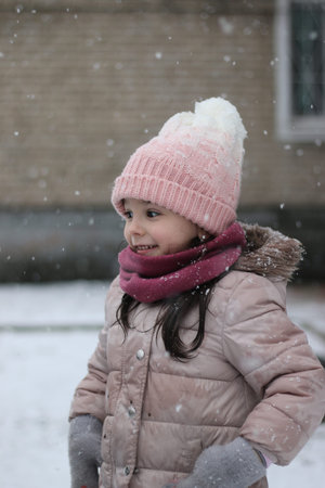Smiling little cute preschooler girl in winter clothes and a pink hat went out to the winter snowy yardの写真素材