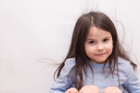 A little preschooler girl with long dark hair and large brown eyes looks in front of her. Studio photo of smiling child on white backgroundの写真素材