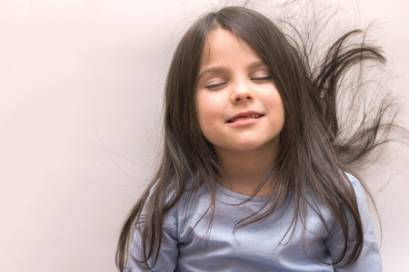 Beautiful little girl with long hair and open mouth on a white background looks down. Preschooler studio shootingの写真素材