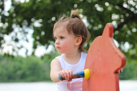 A small child in a white T-shirt on a toy horse on the playground against the background of the river.の写真素材
