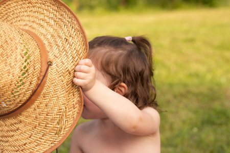 Little girl with a ponytail holding a straw hat in her hand against a blurred rustic backgroundの写真素材