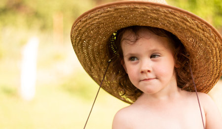 A small, wonderful, focused child in a straw hat holds her by the neckline, looking to the side. Wonderful childhood moments on the farmの写真素材
