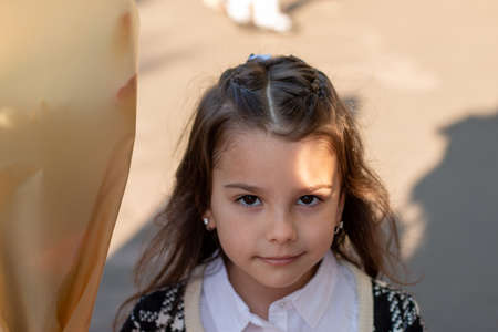 Smiling little girl with long dark hair in a white blouse and a plaid jacket holding a bouquet of flowers in her hand. First-grader's first bell at schoolの写真素材