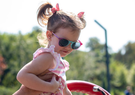 Little beautiful girl in sun-protective glasses with pigtails on the playground