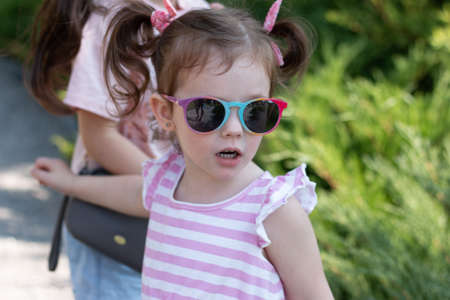 Amazing little girl with ponytails and sunglasses on blurred natural backgroundの写真素材