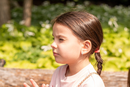 Little beautiful girl with a ponytail squinting looking up while standing on the shore of a pond