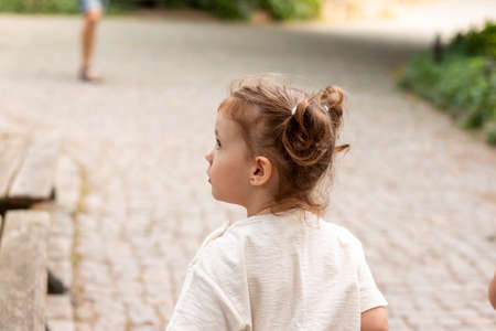 Little cute red-haired girl looks away in surprise while standing on a cobbled roadの写真素材
