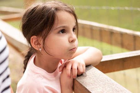 Little beautiful girl with a ponytail leans on the handrail puffing out her cheeksの写真素材