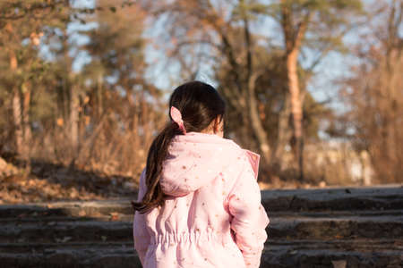 a child with dark hair in a jacket with a fluffy hood climbs the steps in an autumn empty parkの写真素材