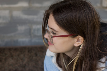 cute hipster teenager girl in glasses sits smiling outdoors