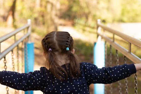 Little beautiful girl with braided pigtails has fun on the uneven bars in the parkの写真素材