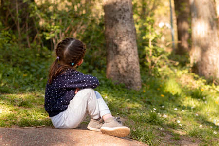 Little beautiful girl sits on a stone surface in a park on a blurred green natural backgroundの写真素材