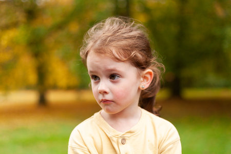 Lovely cute red-haired little girl in the autumn park outdoors