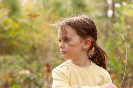 Little blonde girl in a yellow sweatshirt on a walk in autumnの写真素材