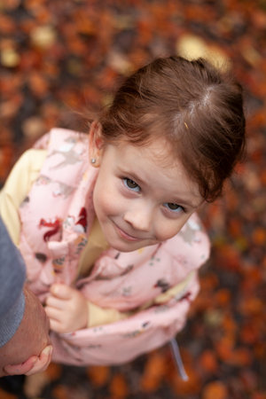 Little cute red-haired girl in a waistcoat smiling looks up. Child on an autumn walk in the parkの写真素材