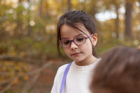 Cute little girl in glasses looking at her mother in autumn park