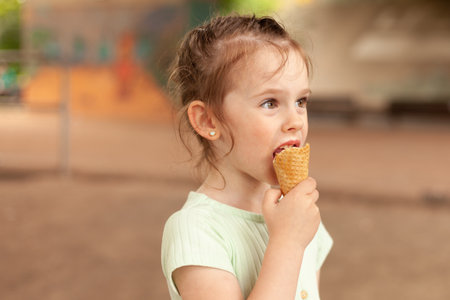 Cute blonde girl in a dress eats an ice cream cone outdoorsの写真素材