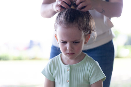 Cute little girl playing with her mother's hair in the parkの写真素材