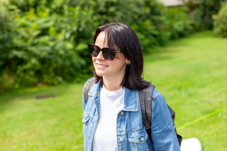 Outdoor portrait of a beautiful young woman in denim jacket wearing sunglasses in the garden