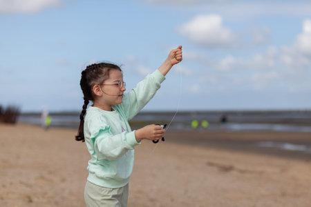 Little girl playing with a fishing rod on the beach in the summerの写真素材