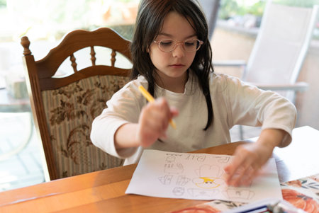 Little girl drawing on a paper at the table in the kitchen.