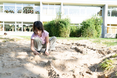 Young girl playing with sand in the garden on a sunny day.の写真素材