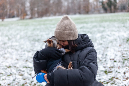 A young mother and her little daughter are walking in the winter park with a cute Yorkshire Terrier dog.の写真素材