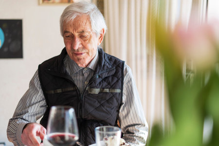 Elderly man sitting at table in restaurant and drinking red wineの写真素材