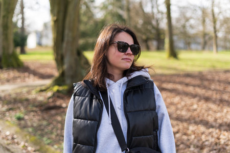 Young woman in sunglasses with backpack walking in a park and looking away