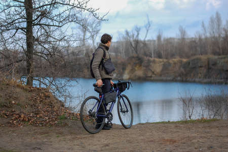 Guy with gravel bike on the shore of the lake on a cloudy autumn day with a backpackの写真素材