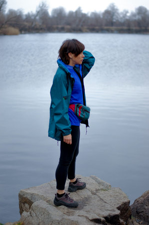 healthy middle-aged woman traveler on the shore of the lake in spring in cloudy weather. hiking....