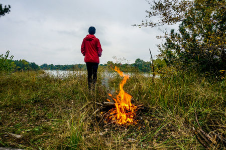 girl by the fire in autumn in a red jacket. trips. hiking