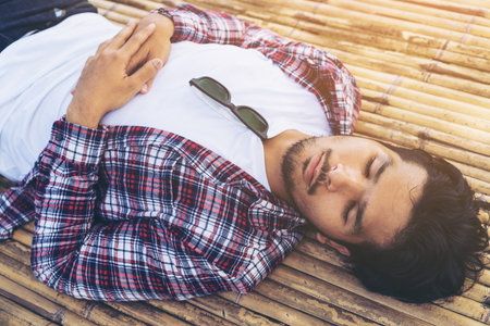 Young man sleep on bamboo bed, seat, table or sunbed made from natural material. Nature, relaxation, and sleep well concept. Daydreamer is daydreaming in day time.の写真素材
