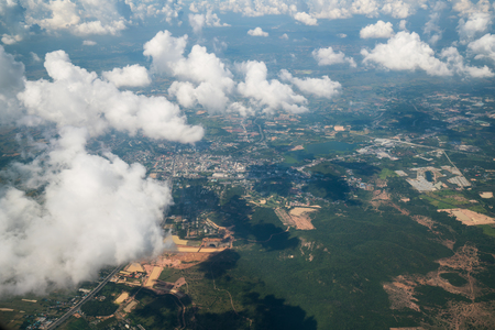 Earth landscape viewed from airplane. Earth surface under the white clouds and blue sky from aerial view. Cloudy weather covering residential land and argriculture land.の写真素材