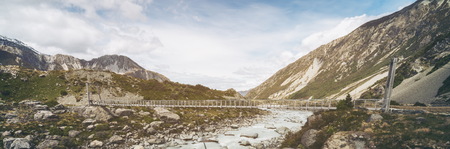 Panorama view of river and mountain landscape with bridge crossing the river. Beautiful nature scenery of rocky terrains. Shot in Mt Cook national park in New Zealand, South Island.の写真素材