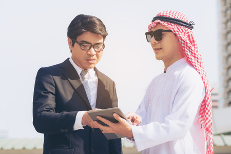 Arab man and businessman discuss content in tablet computer. Multicultural international oversea business meeting.の写真素材