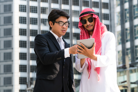 Arab man and businessman discuss content in tablet computer. Multicultural international oversea business meeting.の写真素材