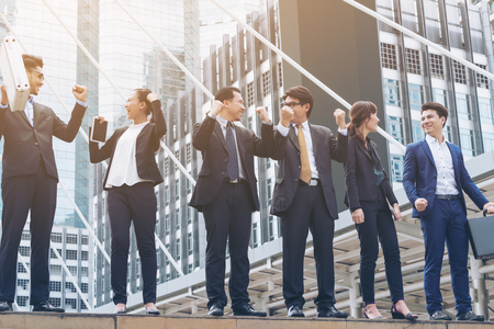 Successful business people stand in line with arms up, city buildings background. Concept of success, collaboration, teamwork and happiness in business.の写真素材