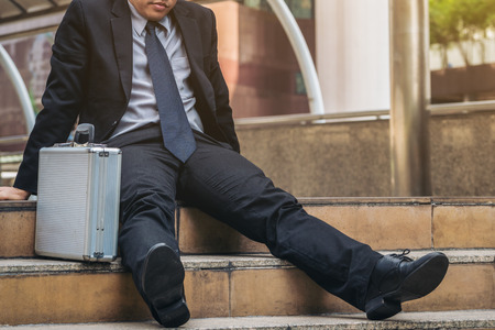 Desperate businessman sitting hopelessly on stair floor in central business district due to unemployment. Concept of failure, desperation, unemployment and business depression.の写真素材